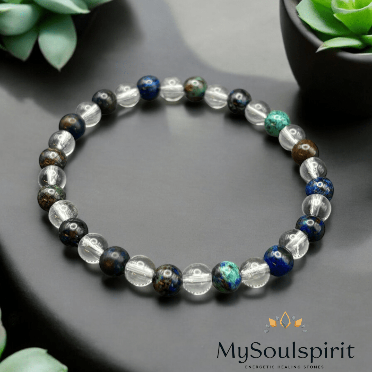 Heilsteinarmband für die Schilddrüse aus Azurit - Malachit - Bergkristall auf einer grauentischplatte mit Pflanzen im Hintergrund.