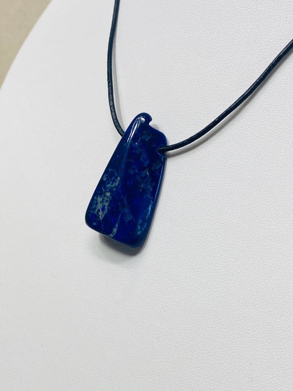 Kettenanhänger aus Lapislazuli als Naturstein an schwarzem Lederband auf weißer Büste