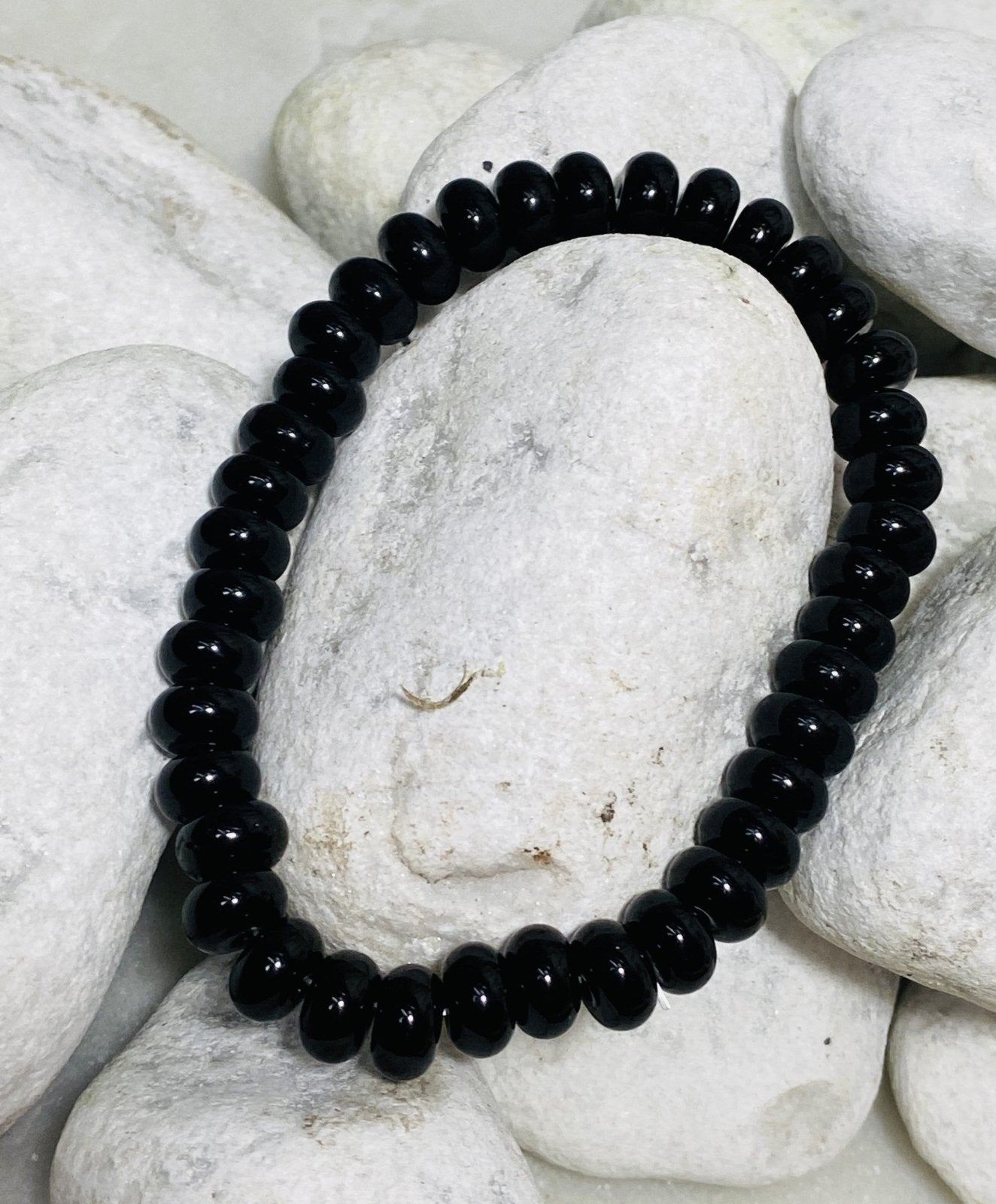 Schwarzes Onyx Button Armband auf weißen Kieselsteinen
