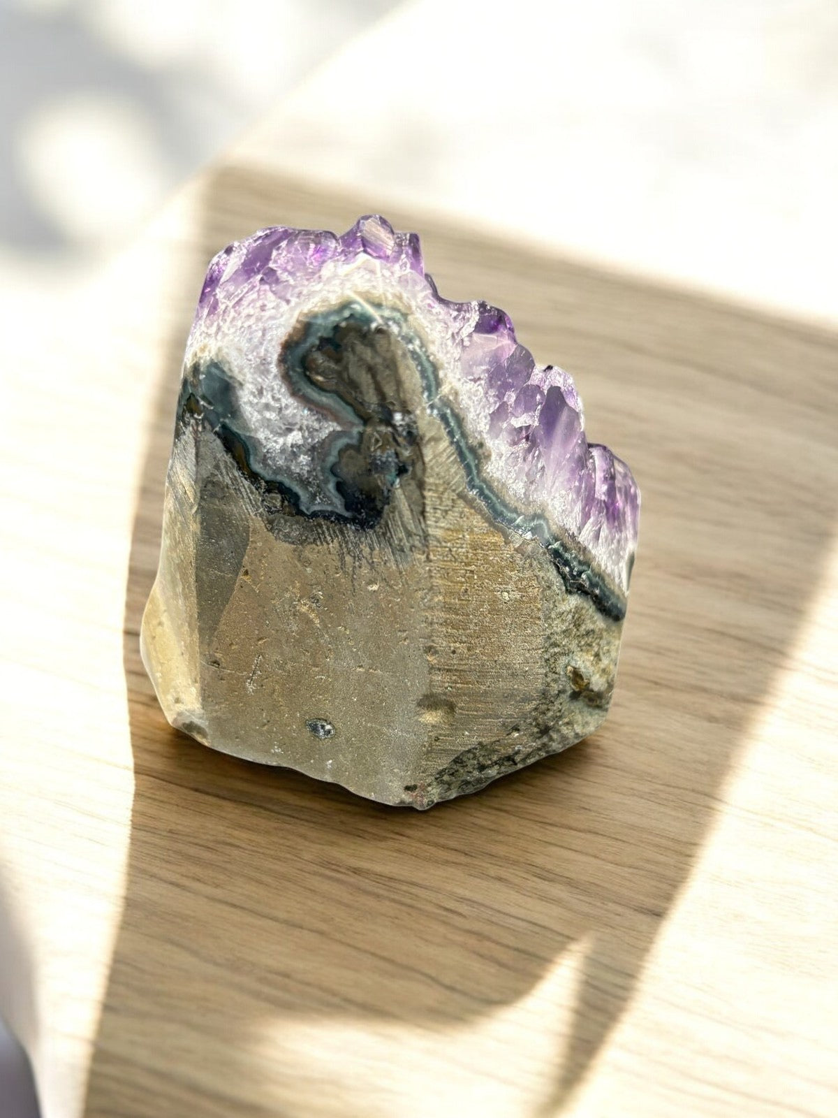 Rückseite der AMethyst Druse auf modernem Holztisch. man erkennt das muttergestein.