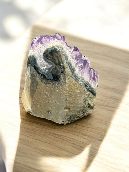 Rückseite der AMethyst Druse auf modernem Holztisch. man erkennt das muttergestein.