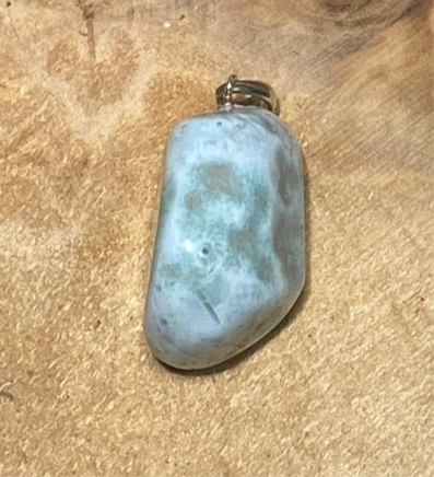 Ein länglicher Larimar Kettenanhänger mit Silberschlaufe für eine Silberkette auf einem Holzbrett. 